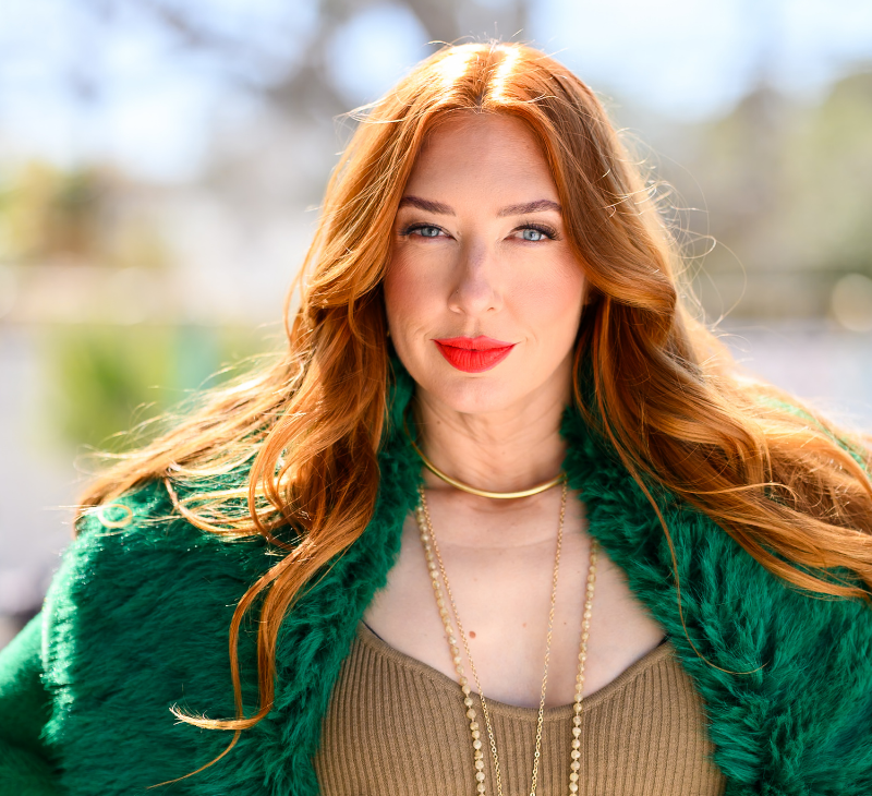 Lesley Logan - Author, Mindset Coach, and Fitness Guru in her green jacket against a bright yellow wall